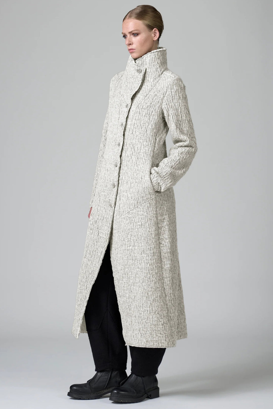 Woman wearing a long, textured coat on a plain background