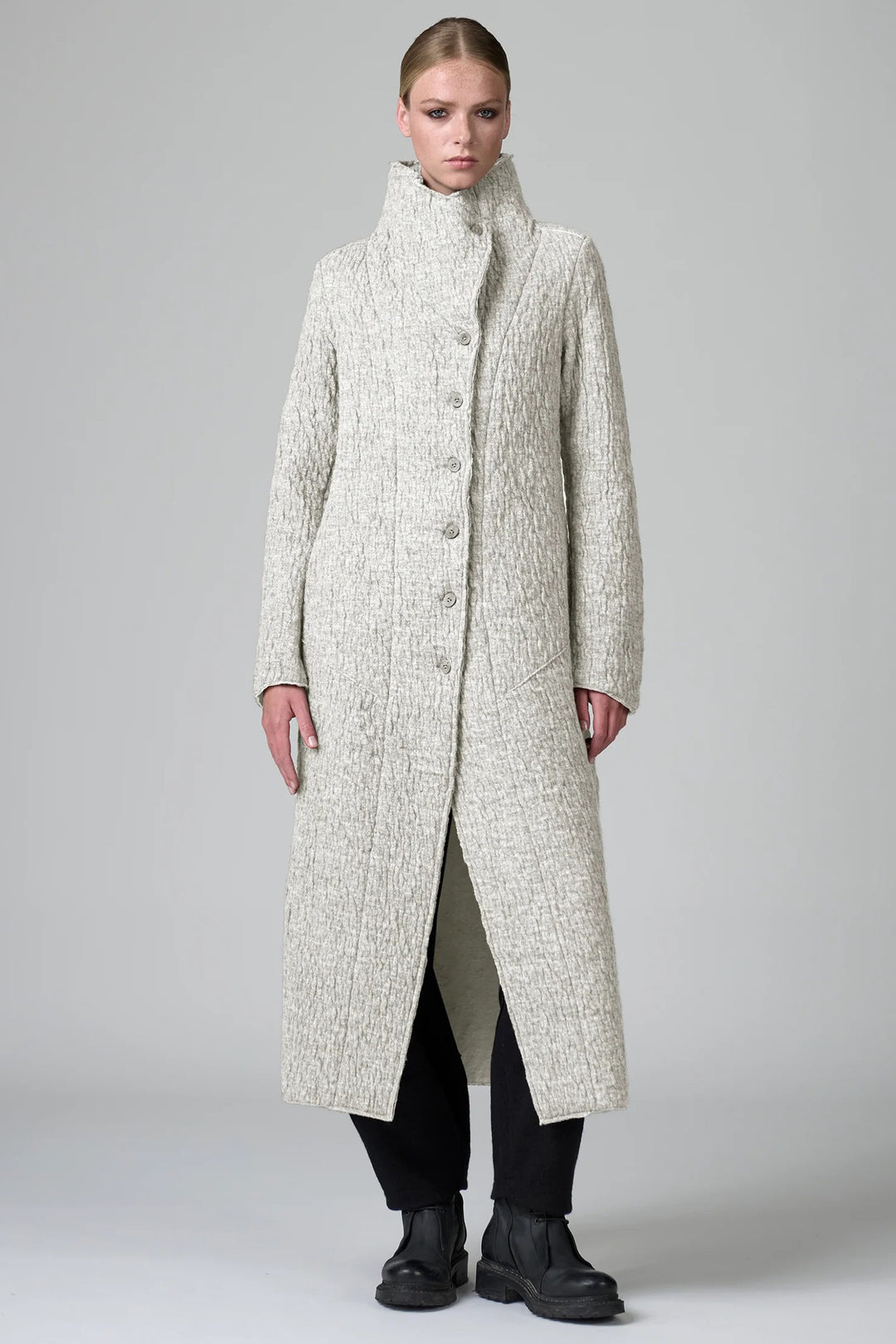 Woman wearing a long, textured coat on a plain background
