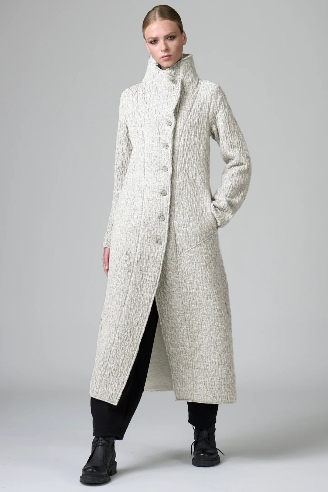 Woman wearing a long, textured coat on a plain background
