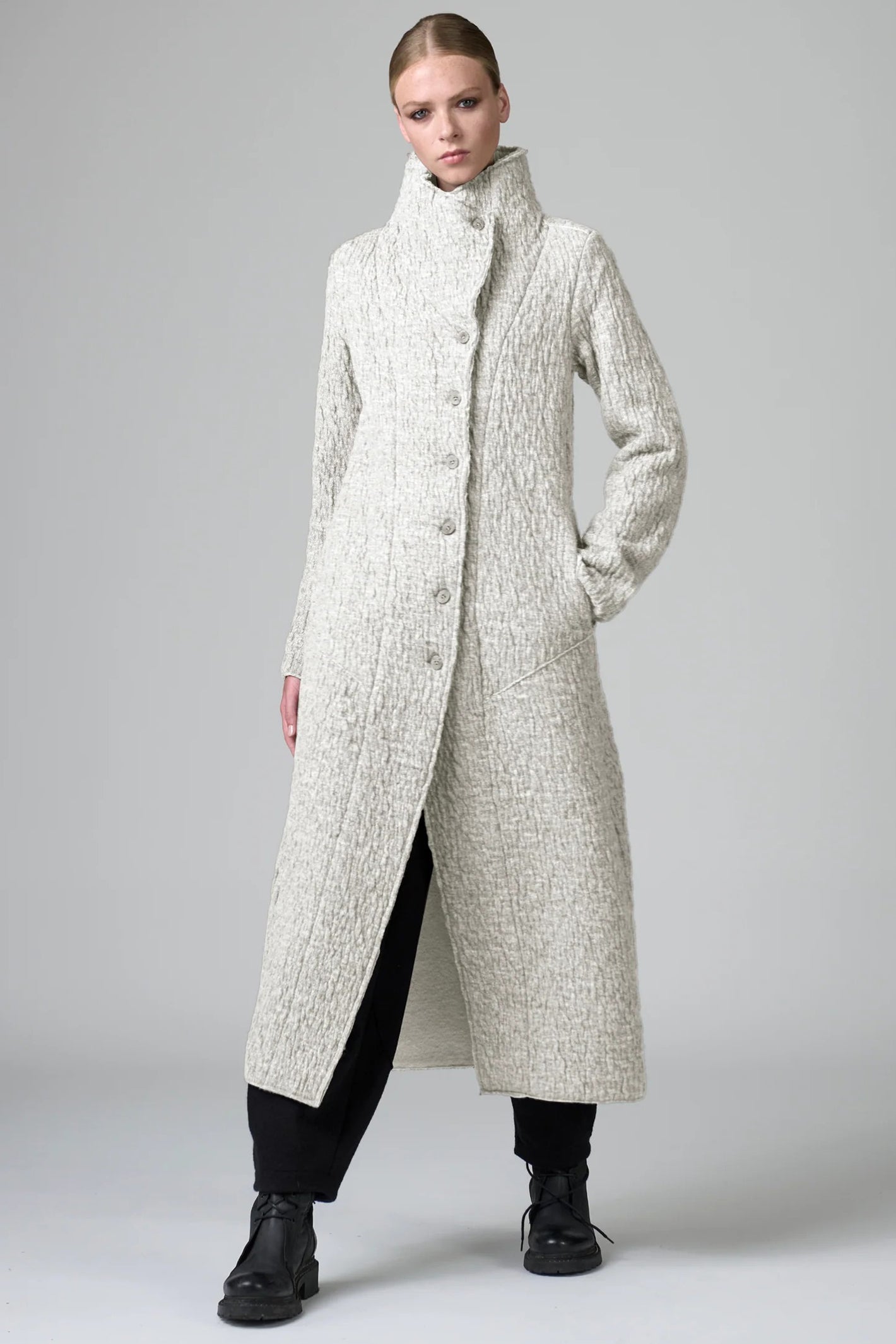 Woman wearing a long, textured coat on a plain background