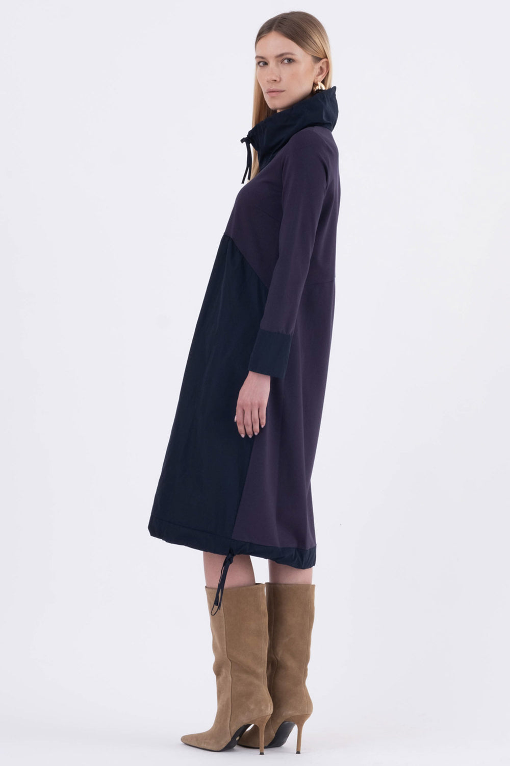 Woman wearing a long dark purple dress with a high collar on a white background